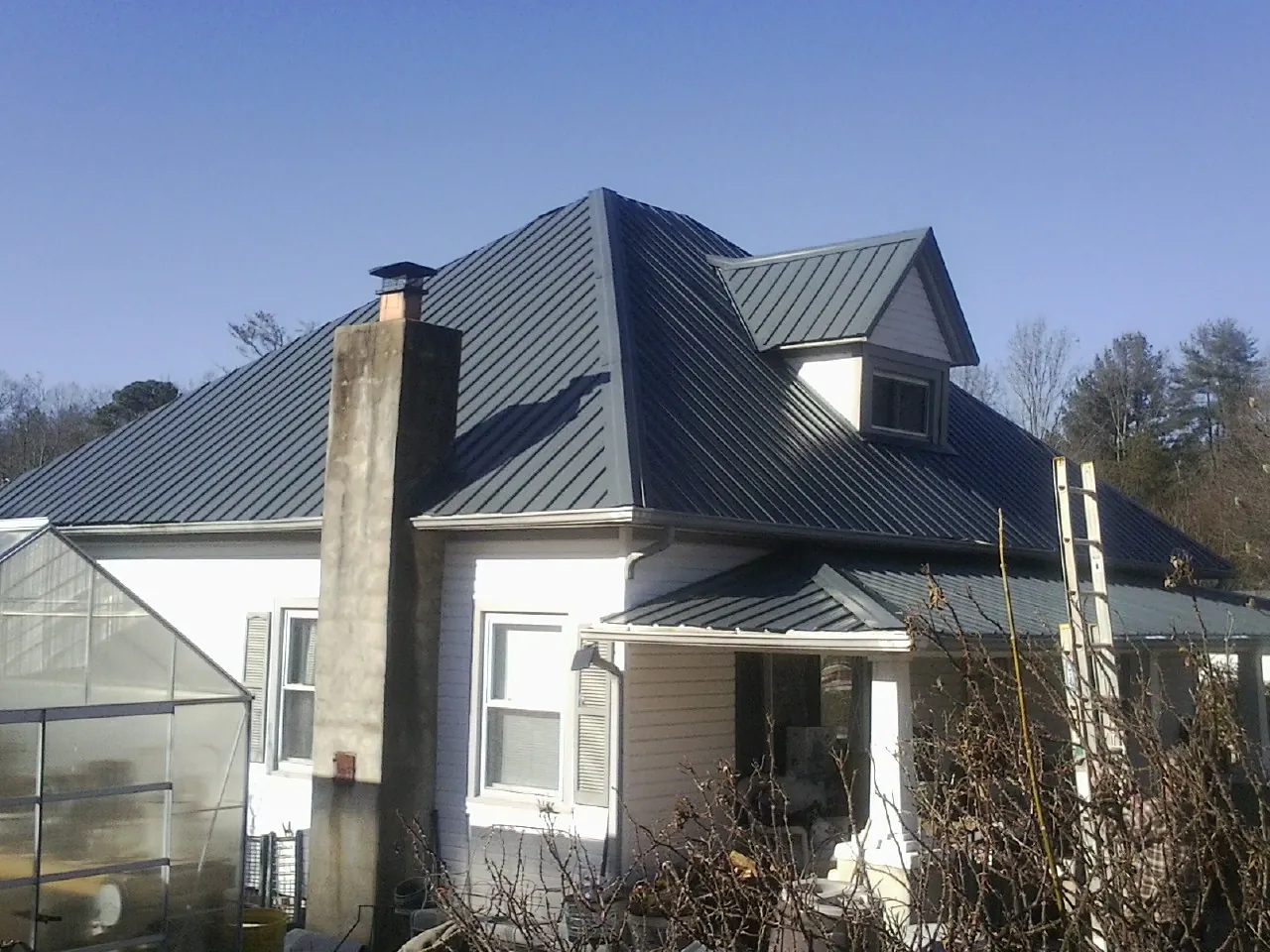 Dark blue standing seam metal roof on a white farmhouse with dormer — Slate & Tile Roof Repair by Roofing Brothers in Bly
