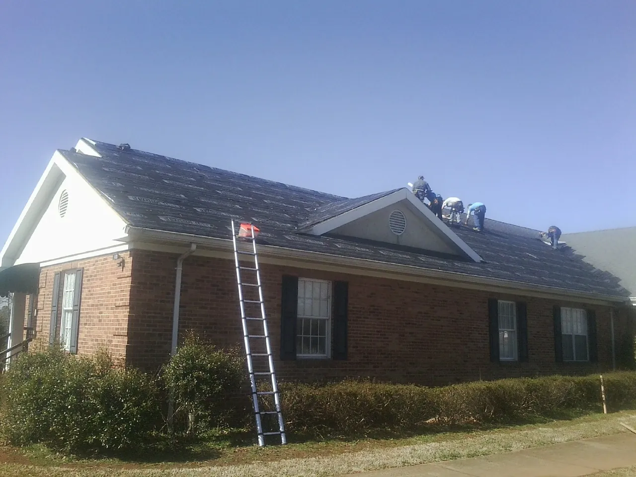 Crew tearing shingles off a brick ranch roof with a ladder set — Metal Roof Repair work by our crew in Bly