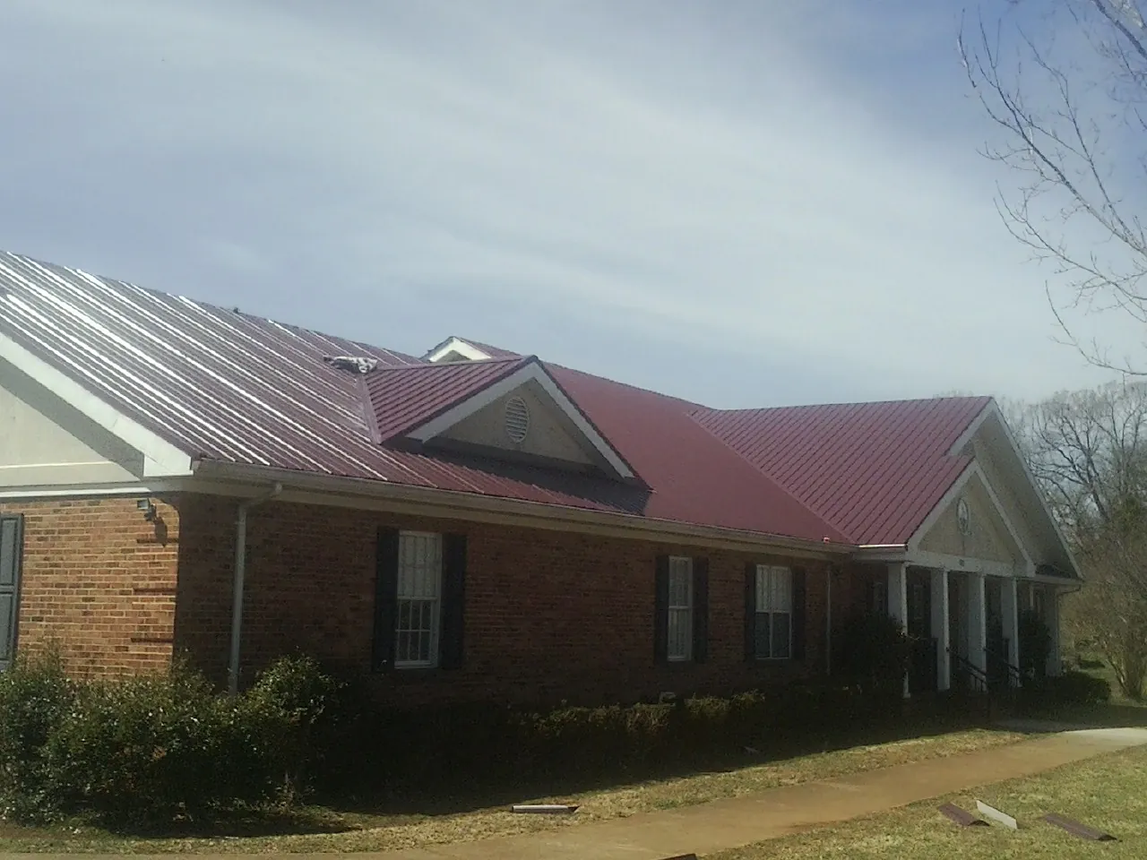 Red metal roof with gabled entries on a long brick building, from a Hail Damage Roof Repair job in Bly