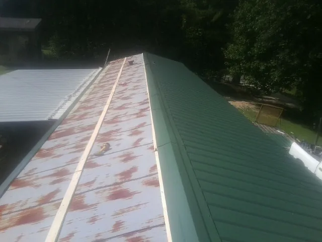 Old rusted panels beside newly installed green metal roofing — Wind Damage Roof Repair by Roofing Brothers in Bly