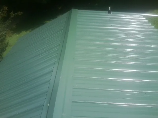 New green metal panels meeting at the ridge of a roof — Flat Roof Repair work by our crew in Bly