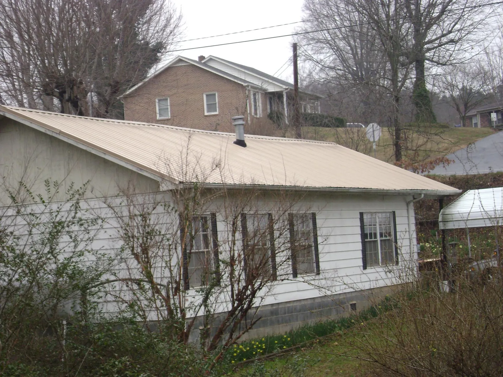 Tan metal roof on a white sided house set into a hillside — Commercial Roofing by Roofing Brothers in Bly